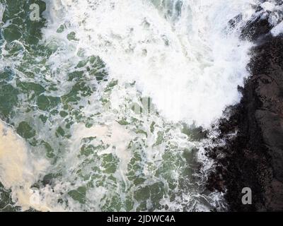 Vue de dessus de l'océan qui fait rage. Des vagues de mousse blanche s'écrasont contre le rivage. Abstraction. Minimalisme. Beauté de la faune, protection de l'environnement, géologie, Banque D'Images