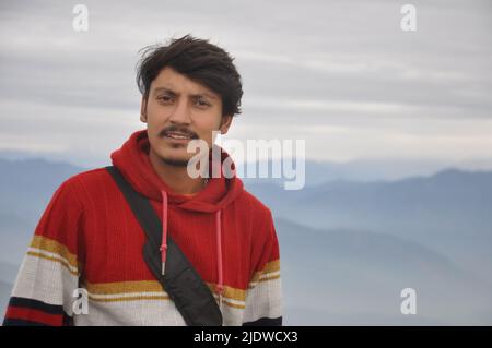 Gros plan d'un jeune garçon indien beau regardant la caméra tout en se tenant contre le fond des montagnes Banque D'Images