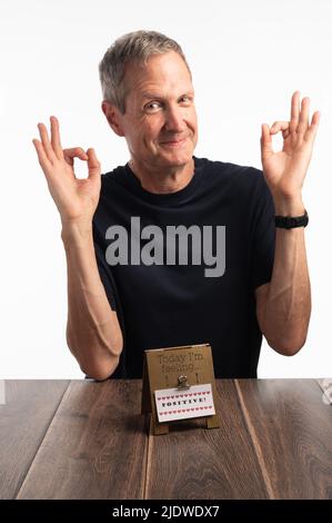 Un homme souriant, beau, âgé, dans un tee-shirt bleu avec les deux mains vers le haut, signalisation OK, sur fond blanc. Banque D'Images