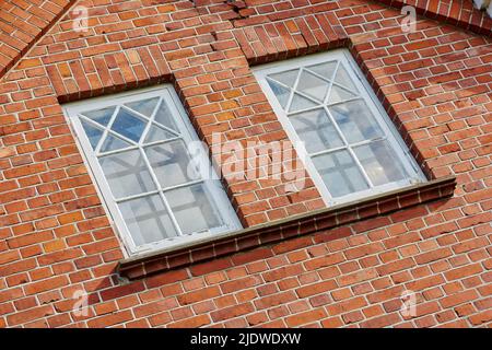 Vieux mur en pierre avec deux fenêtres rectangulaires. Gros plan des fenêtres rectangulaires d'un bâtiment avec un mur de briques rouges. Fenêtres à motifs colorées en rouge Banque D'Images