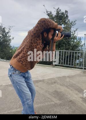 Vue latérale d'un jeune photographe à poil long et barbu qui prend des photos avec un appareil photo reflex numérique tout en étant debout à l'extérieur Banque D'Images