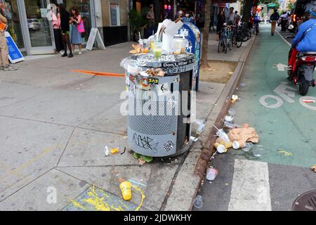 Une poubelle débordante avec détritus sur le trottoir près d'un coin de rue sur St. Marks PL. Dans le quartier East Village de Manhattan à New York. Banque D'Images