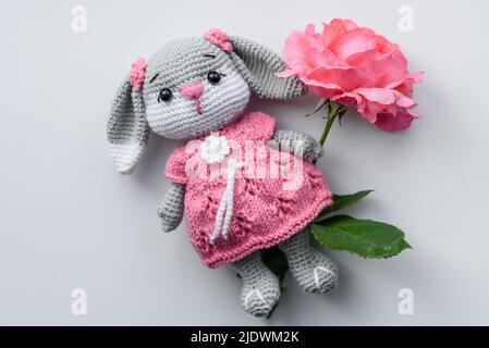 Magnifique jouet de lapin tricoté avec des beignets à la glaçure rose et saupoudrés de couleur sur un fond de béton foncé Banque D'Images