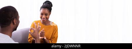 Smiling Young Couple Sitting on Sofa Communication avec les langues des signes Banque D'Images