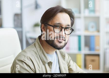 Portrait de contenu beau jeune barbu asiatique gars en lunettes de vue travaillant dans le bureau moderne Banque D'Images