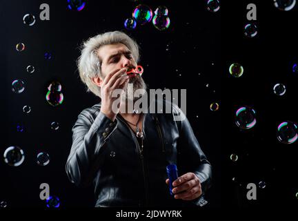 Homme barbu soufflant des bulles de savon. Bonne humeur. Concept d'enfance et de bonheur. Jouer avec la bulle. Banque D'Images