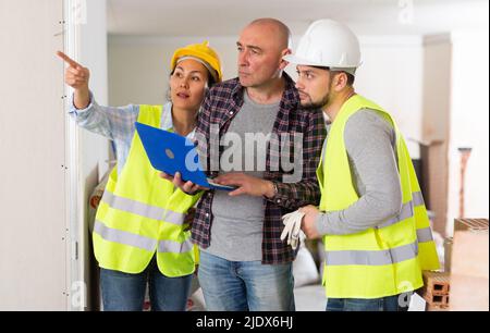 Propriétaire avec ordinateur portable discutant de la rénovation de la maison avec les constructeurs Banque D'Images