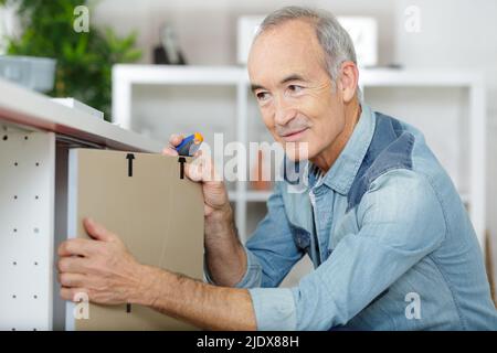 homme senior assemblant un placard de base de cuisine Banque D'Images