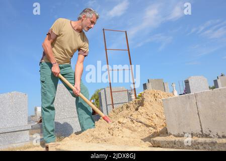 Homme en pelant du sable dans un cimetière Banque D'Images