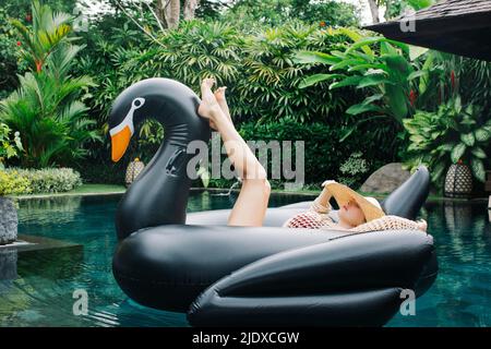 Jeune femme se détendant sur un flotteur en forme de cygne Banque D'Images