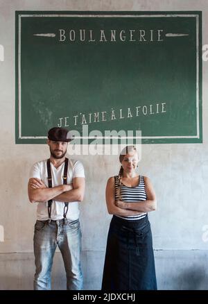 Les propriétaires de boulangerie confiants debout avec les bras croisés devant le mur avec le texte français Banque D'Images