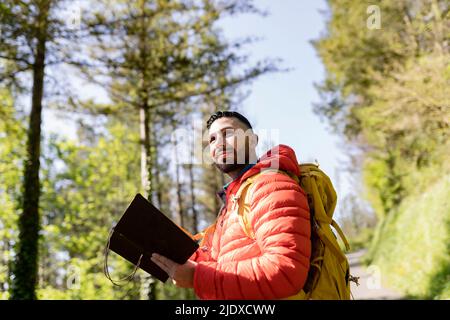 Homme portant un sac à dos debout avec un journal dans la forêt le jour ensoleillé Banque D'Images