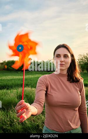 Jeune femme tenant le jouet de roue d'épingle sur le pique-nique dans le champ au coucher du soleil Banque D'Images