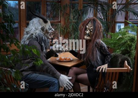 Homme et femme en costume effrayant toaster les verres à vin assis à table Banque D'Images