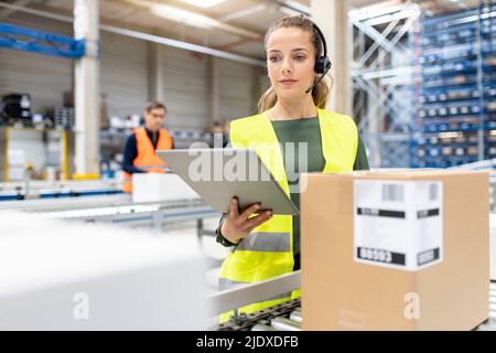 Jeune travailleur avec un PC tablette examinant des boîtes en carton dans l'entrepôt Banque D'Images