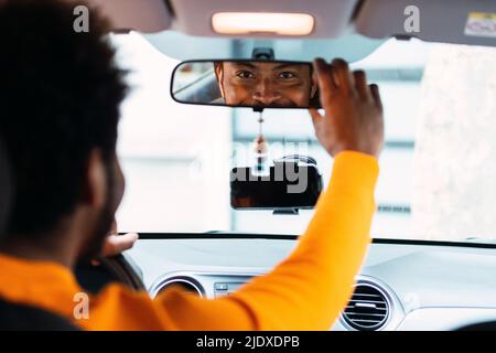 Homme souriant regardant dans le rétroviseur de la voiture Banque D'Images