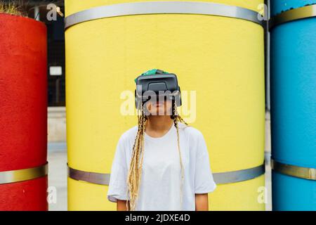 Jeune femme portant un simulateur de réalité virtuelle debout devant un tuyau en béton jaune Banque D'Images
