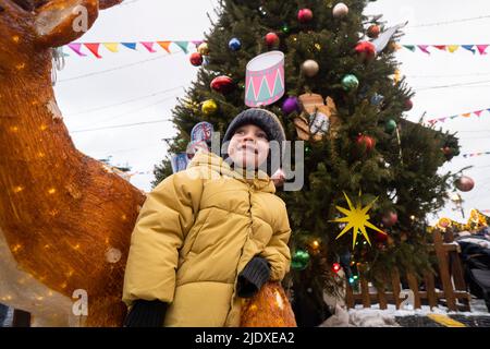 Garçon avec chapeau en tricot debout par la décoration de cerf dans le marché de Noël Banque D'Images