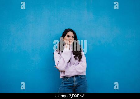 Jeune femme attentionnée debout devant le mur bleu Banque D'Images