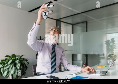 Homme d'affaires examinant robot jouet assis avec un ordinateur portable au bureau Banque D'Images