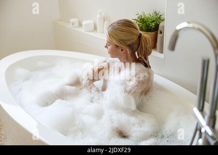 Belle jeune femme blonde se lavant elle-même et en train de se saliver tout en prenant le bain. Banque D'Images