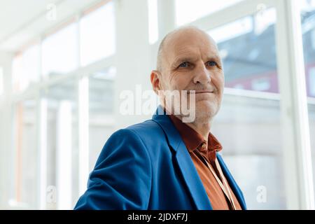 Homme d'affaires souriant portant un blazer bleu au bureau Banque D'Images