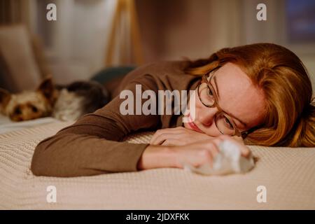 Femme triste et attentionnés avec du papier de soie couché par un chien d'animal de compagnie sur le lit à la maison Banque D'Images