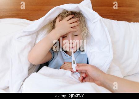 La mère prend soin de sa fille malade et utilise un thermomètre sur le lit Banque D'Images