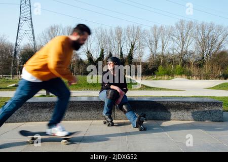 Un homme mûr patinant par un ami assis dans le parc Banque D'Images