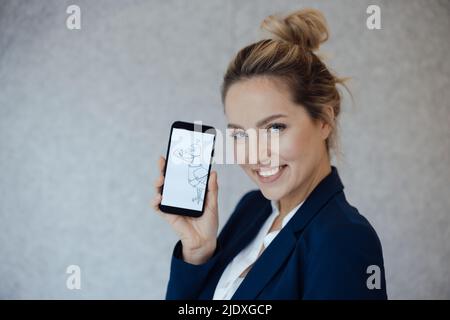 Bonne femme d'affaires montrant le pigeon sur l'écran du smartphone devant le mur gris Banque D'Images