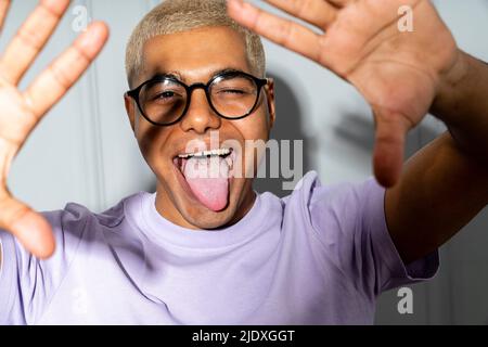 Jeune homme portant des lunettes qui dépassent de la langue Banque D'Images