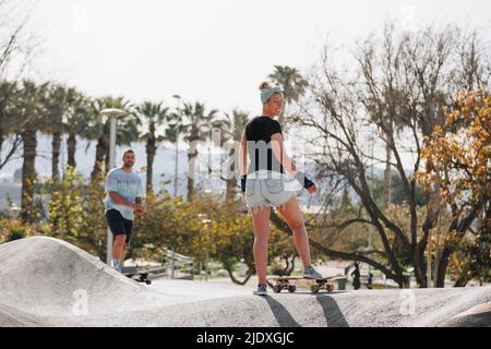 Femme souriante avec planche à roulettes devant un ami sur la rampe de sport Banque D'Images