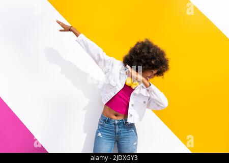 Jeune Afro ludique qui fait de la danse dab devant un mur coloré Banque D'Images