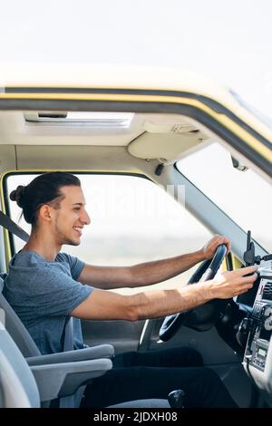 Jeune homme heureux utilisant un téléphone portable assis dans une camionnette Banque D'Images