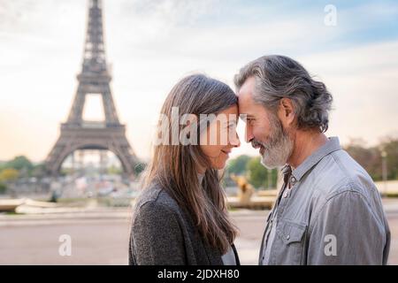 Couple d'âge mûr souriant touchant les fronts en face de la Tour Eiffel, Paris, France Banque D'Images