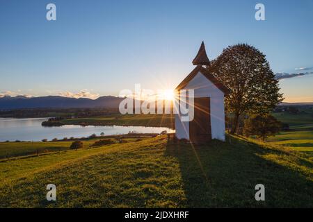 Allemagne, Bavière, Aidling, Mesnerhauskapelle au coucher du soleil avec le lac Riegsee en arrière-plan Banque D'Images