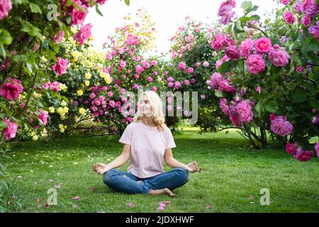 Femme avec les yeux fermés méditant au milieu du jardin de roses Banque D'Images