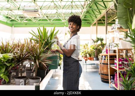 Un jardinier souriant tenant l'arrosage peut se tenir près des plantes à la pépinière Banque D'Images