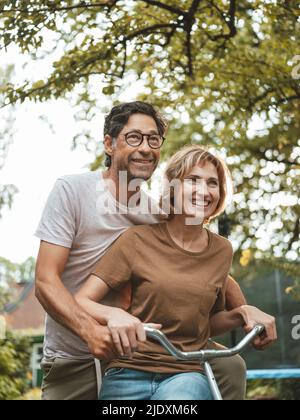 Heureux homme mature et femme à vélo ensemble dans la cour arrière Banque D'Images