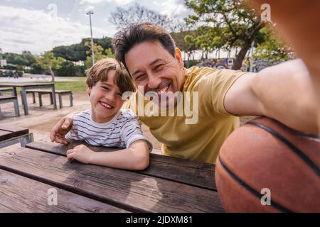 Homme gai avec son fils prenant le selfie le jour ensoleillé Banque D'Images