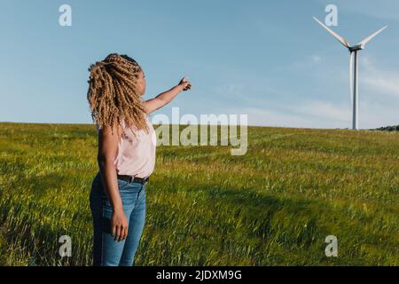 Jeune femme pointant vers un moulin à vent debout dans un pré Banque D'Images