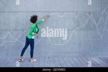 Jeune femme pointant sur un tableau peint sur le mur Banque D'Images