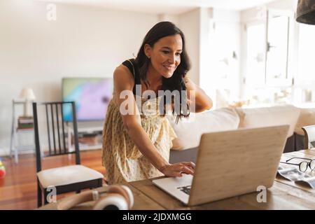 Femme enceinte souriante utilisant un ordinateur portable travaillant à la maison Banque D'Images