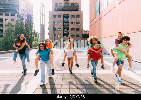 Des filles et des garçons joyeux qui offrent une promenade en porcgyback à des amis le jour ensoleillé Banque D'Images