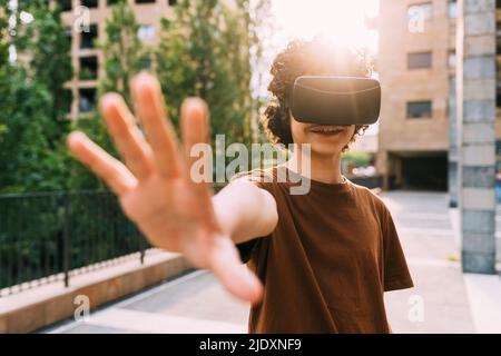 Jeune garçon souriant portant un simulateur de réalité virtuelle en train de gesturer Banque D'Images