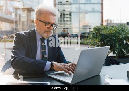 Homme d'affaires senior travaillant sur un ordinateur portable assis à l'extérieur Banque D'Images