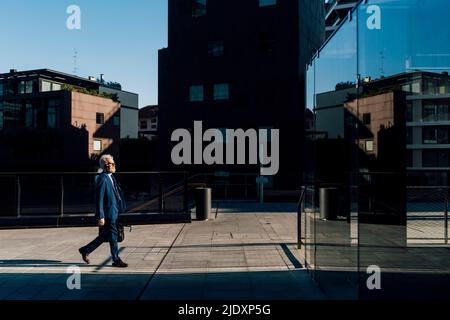 Un homme d'affaires de premier plan se promenant devant un immeuble de bureaux par beau temps Banque D'Images