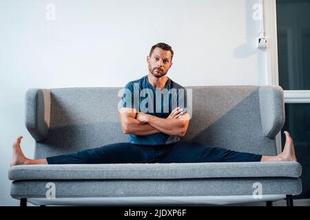 Homme étirant les jambes assis avec les bras croisés sur le canapé à la maison Banque D'Images