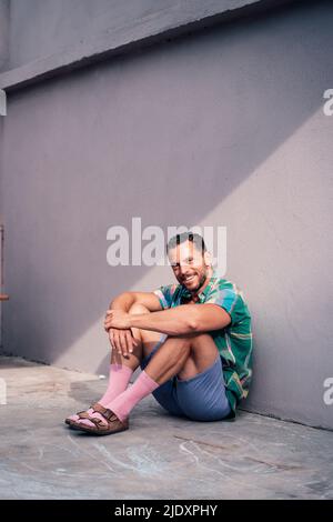 Homme souriant assis sur le sol près du mur Banque D'Images