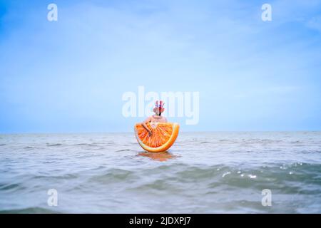 Homme portant une tranche d'orange gonflable debout en mer Banque D'Images